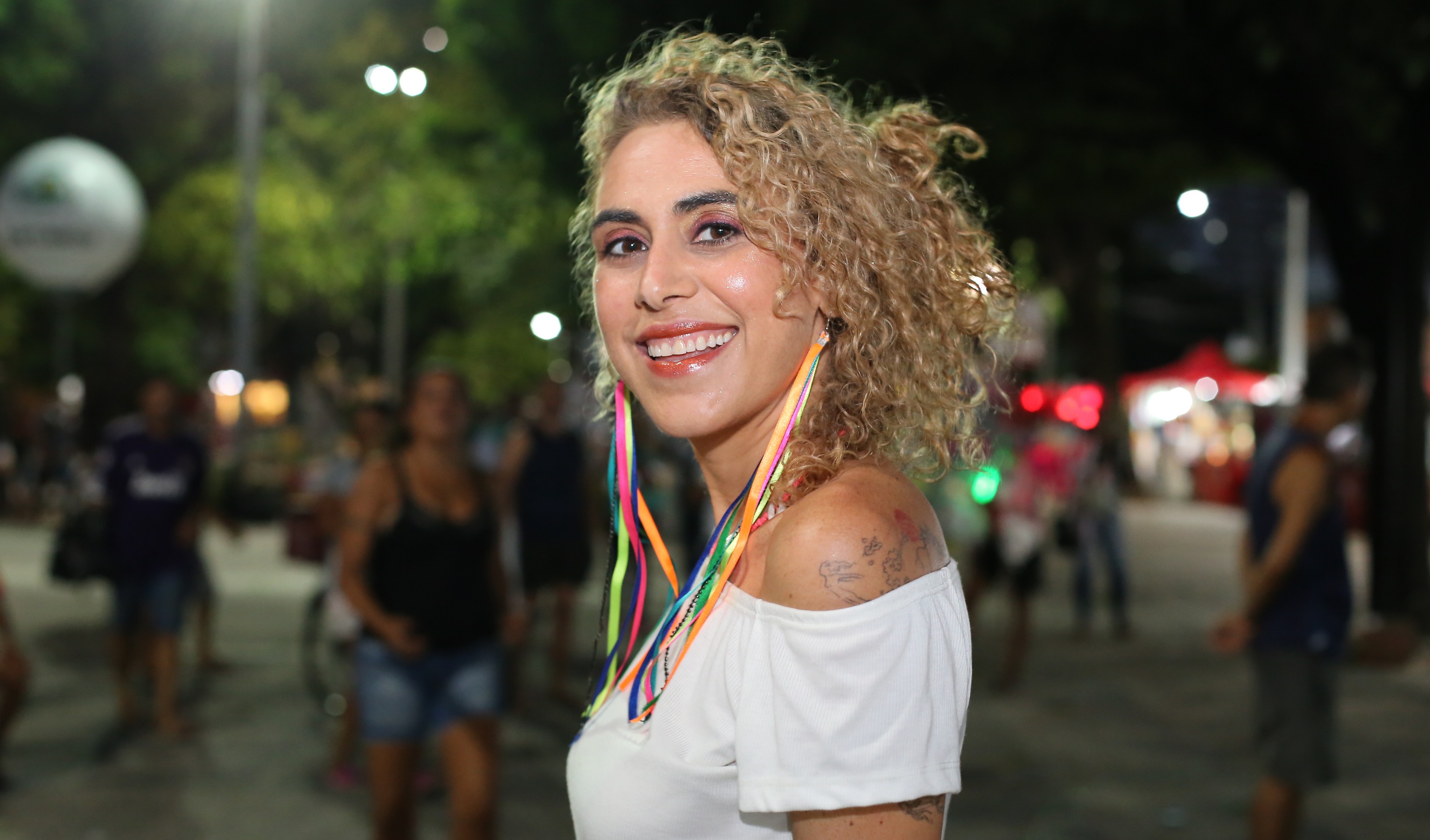 mulher com adereços carnavalescos de perfil sorrindo para a foto